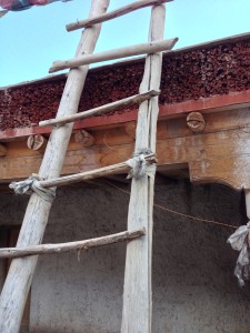A wooden ladder leading to a roof portion of the monastery at Sumdo. Rickety for a 90 kg person, it includes tied cloth reinforced rungs that experience as the ladder sits just feet from the edge of the roof line, and a valley far below.